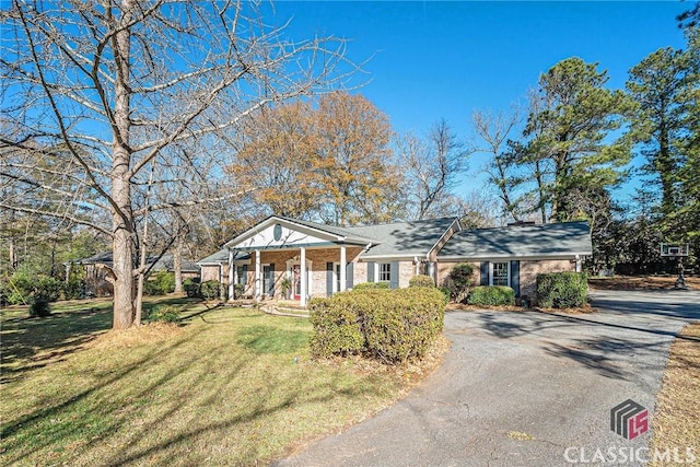 greek revival inspired property with covered porch, brick siding, aphalt driveway, and a front yard