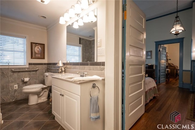 bathroom featuring toilet, hardwood / wood-style flooring, vanity, tile walls, and ornamental molding