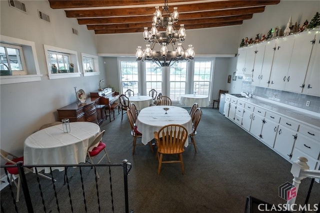 carpeted dining room with beamed ceiling, plenty of natural light, sink, and a chandelier