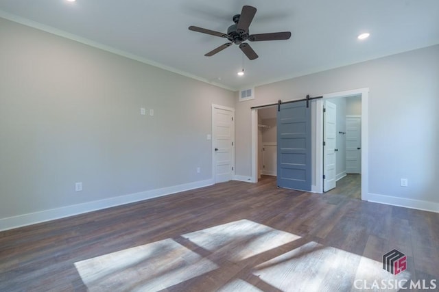 unfurnished bedroom featuring dark wood-type flooring, a spacious closet, a closet, ceiling fan, and a barn door