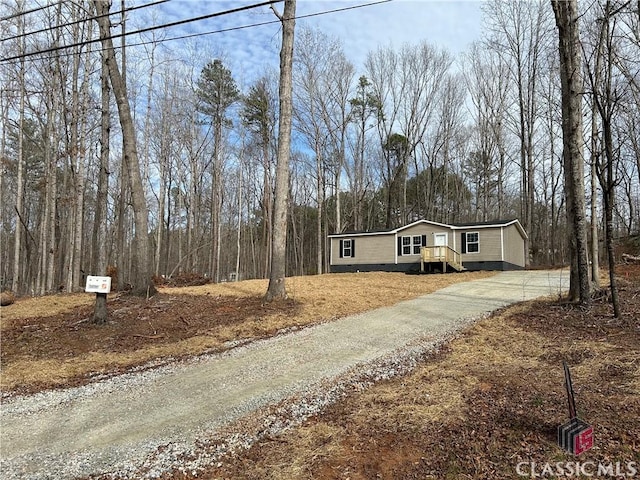 view of front of property featuring crawl space, a view of trees, and driveway