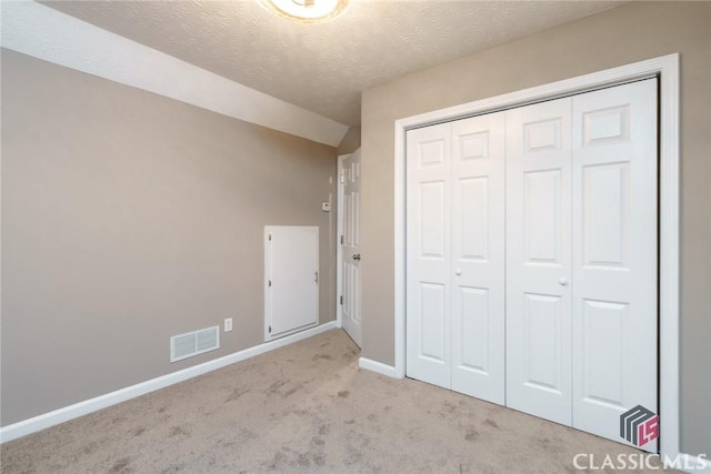 unfurnished bedroom featuring a textured ceiling, a closet, light carpet, and vaulted ceiling