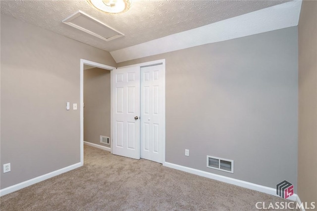 unfurnished bedroom with light colored carpet, a closet, vaulted ceiling, and a textured ceiling