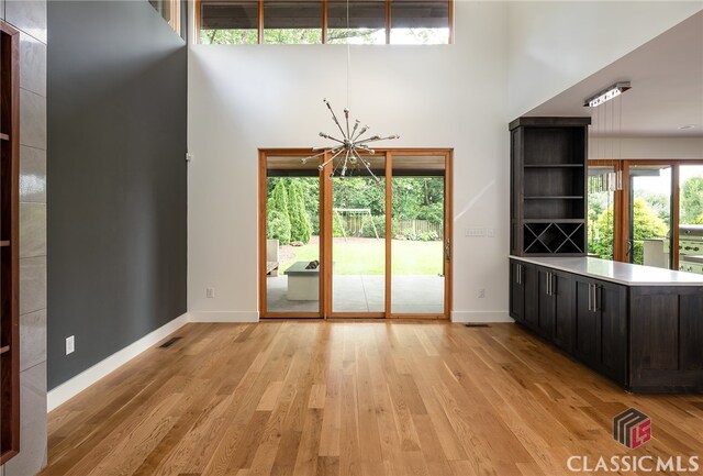 unfurnished dining area featuring a towering ceiling, light hardwood / wood-style floors, and an inviting chandelier