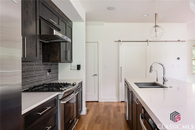 kitchen with decorative backsplash, appliances with stainless steel finishes, sink, pendant lighting, and light hardwood / wood-style floors