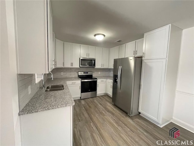 kitchen featuring hardwood / wood-style floors, white cabinets, sink, decorative backsplash, and stainless steel appliances