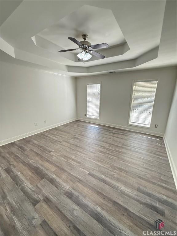 empty room with dark hardwood / wood-style floors, ceiling fan, and a raised ceiling