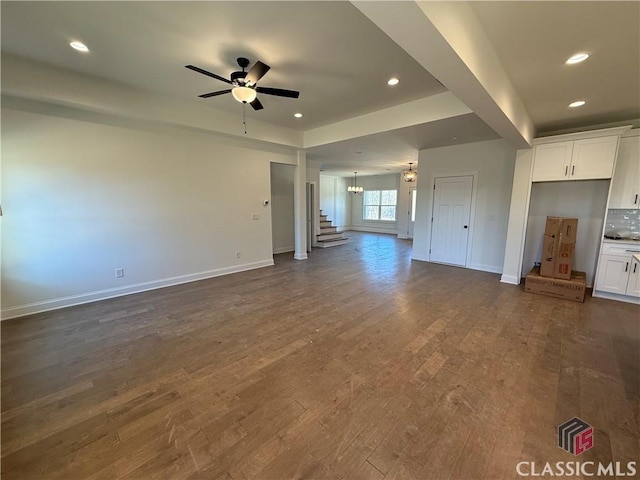 unfurnished living room featuring ceiling fan with notable chandelier and dark hardwood / wood-style flooring