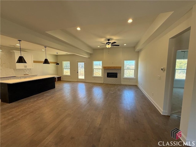 unfurnished living room featuring ceiling fan, dark hardwood / wood-style flooring, a brick fireplace, and a wealth of natural light