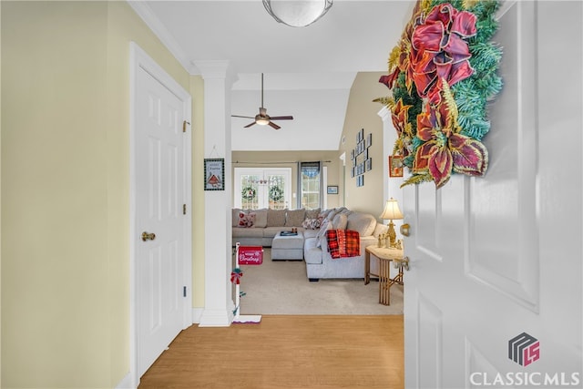 corridor with light hardwood / wood-style floors, lofted ceiling, and ornamental molding