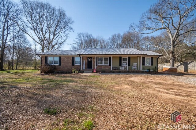 single story home featuring covered porch, brick siding, and metal roof