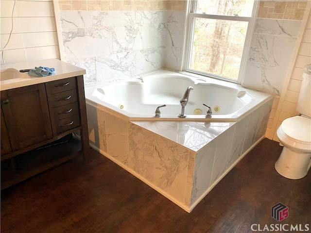 bathroom featuring tile walls, hardwood / wood-style floors, tiled bath, and toilet