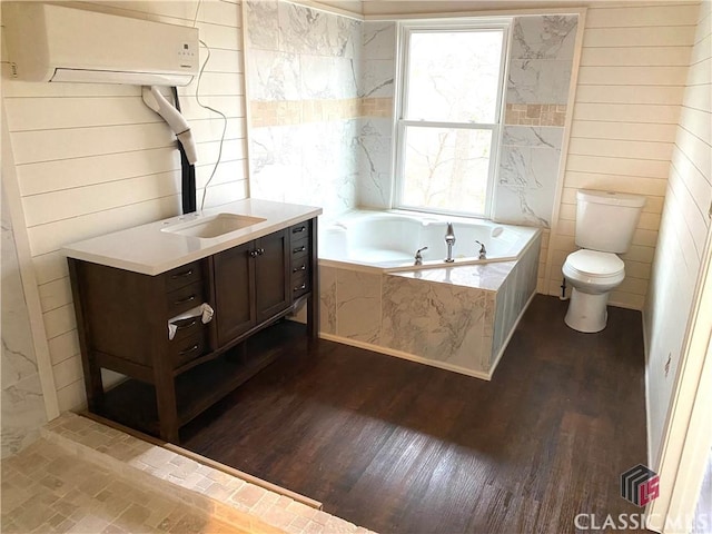 bathroom featuring hardwood / wood-style flooring, tiled bath, toilet, a wall mounted AC, and vanity