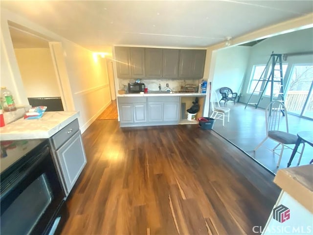 kitchen featuring black electric range, gray cabinets, dark wood-type flooring, sink, and backsplash