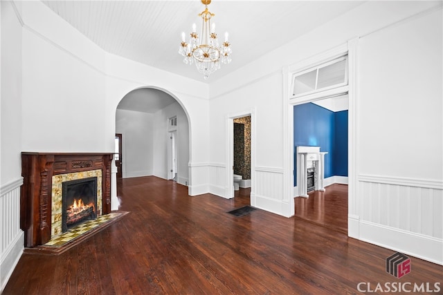 unfurnished living room with a fireplace with flush hearth, arched walkways, visible vents, a chandelier, and wood finished floors