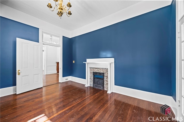 unfurnished living room with baseboards, wood finished floors, a fireplace, and a chandelier