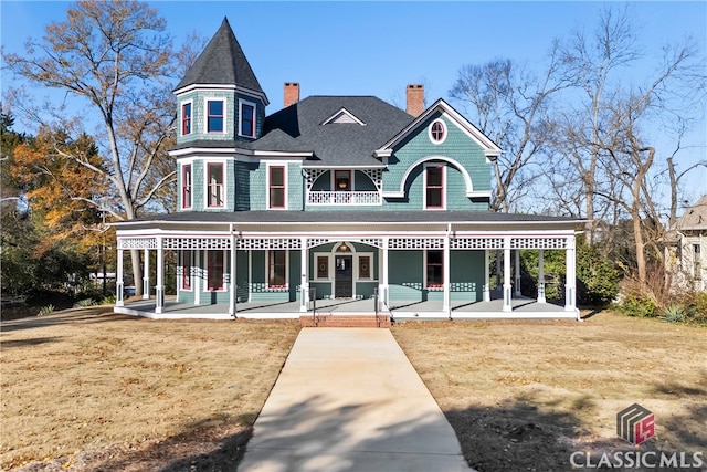 back of house with a lawn, a shingled roof, a chimney, and covered porch