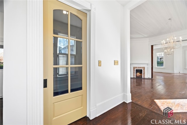 foyer featuring baseboards, an inviting chandelier, a warm lit fireplace, and dark wood-style flooring