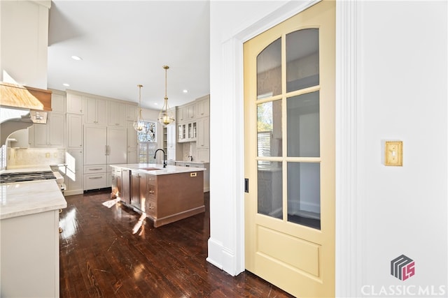 kitchen with a kitchen island with sink, a sink, recessed lighting, pendant lighting, and dark wood-type flooring