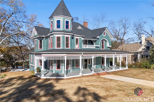 back of property with a porch, a shingled roof, and a yard
