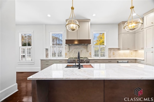 kitchen featuring light stone counters, a sink, an island with sink, backsplash, and dark wood-style flooring