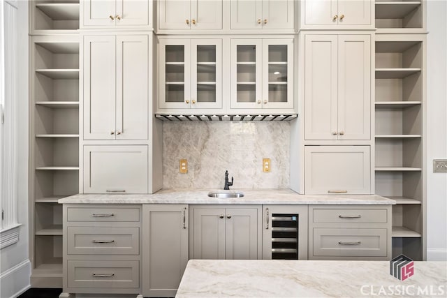 bar with decorative backsplash, beverage cooler, baseboards, and a sink
