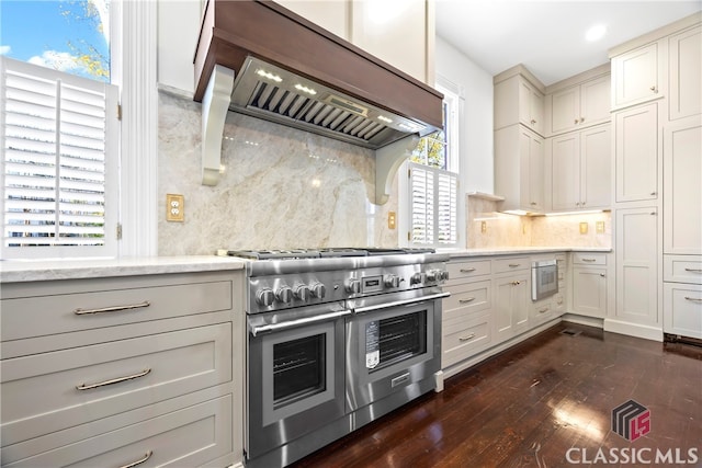 kitchen with custom exhaust hood, tasteful backsplash, range with two ovens, light stone countertops, and dark wood-style floors