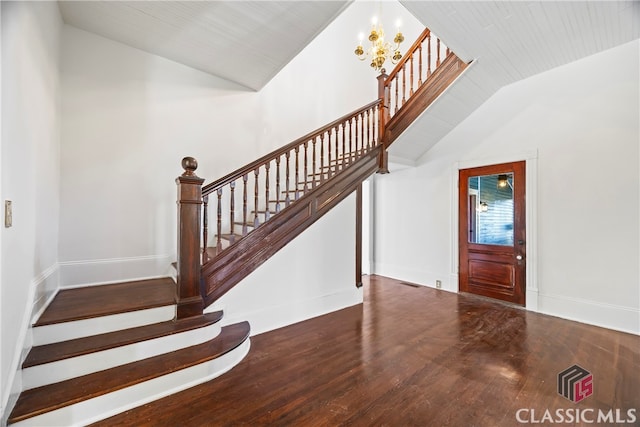 foyer with lofted ceiling, wood finished floors, a notable chandelier, and stairway