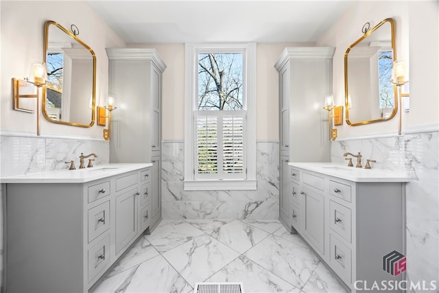 bathroom featuring marble finish floor, a wainscoted wall, two vanities, and tile walls