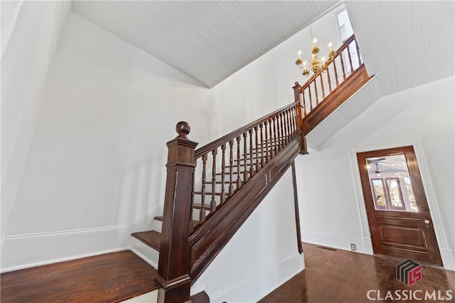 staircase with a chandelier, vaulted ceiling, baseboards, and wood finished floors