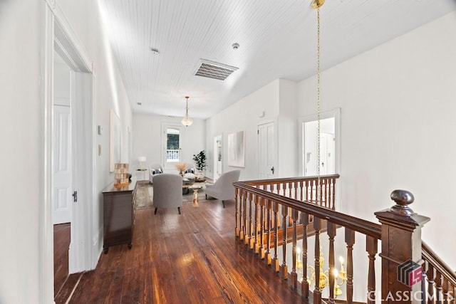 hall with dark wood-type flooring, visible vents, and an upstairs landing
