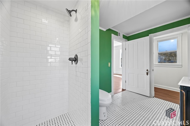 bathroom with a tile shower, toilet, and ornamental molding