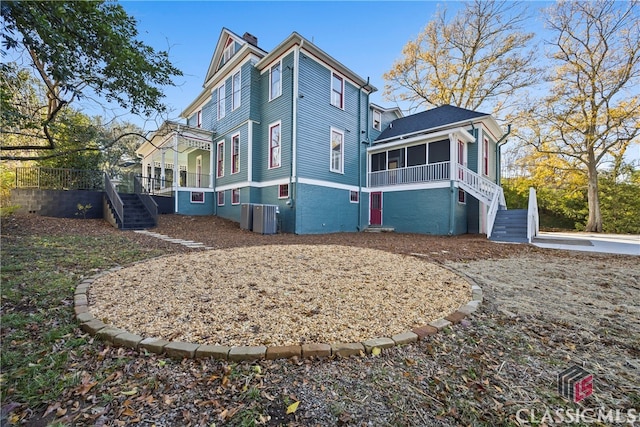 back of house featuring a chimney, central AC unit, a sunroom, and stairs
