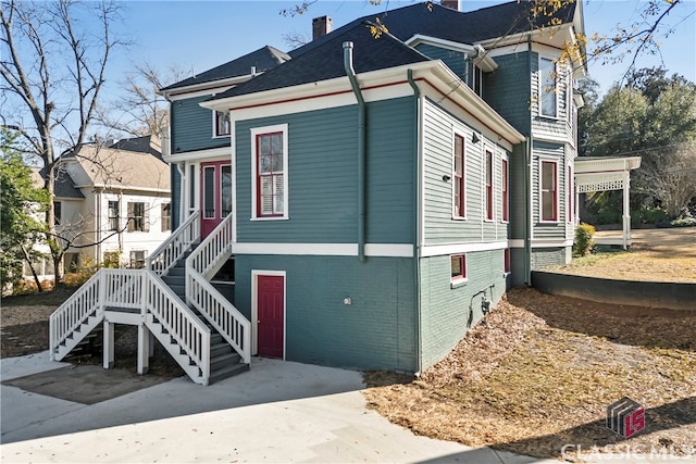 view of front of property featuring a chimney, stairway, and brick siding