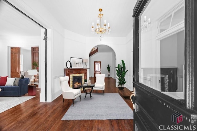living area featuring arched walkways, dark wood finished floors, a brick fireplace, and a notable chandelier