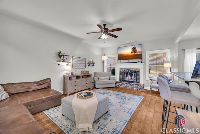 living room featuring ceiling fan, a brick fireplace, wood finished floors, and baseboards