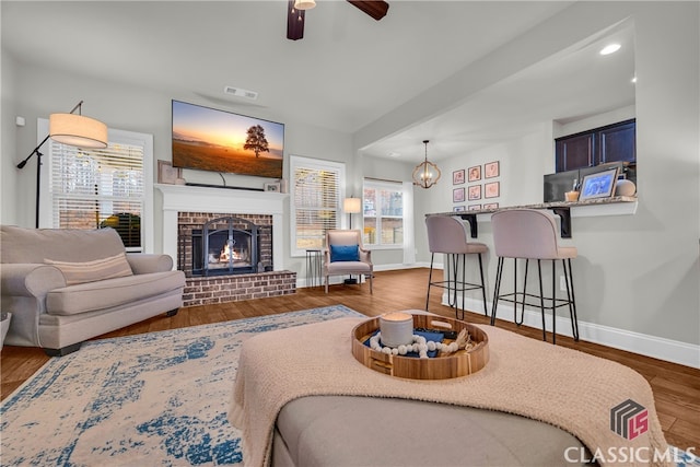 living room featuring a fireplace, visible vents, a ceiling fan, wood finished floors, and baseboards