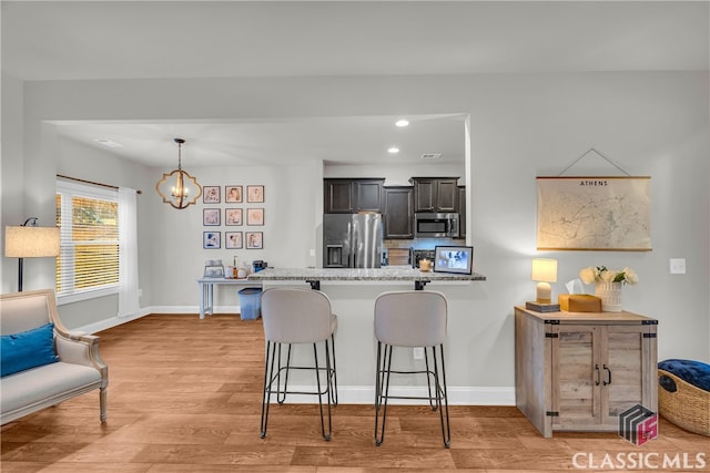 kitchen featuring light wood-style flooring, appliances with stainless steel finishes, a breakfast bar, and baseboards