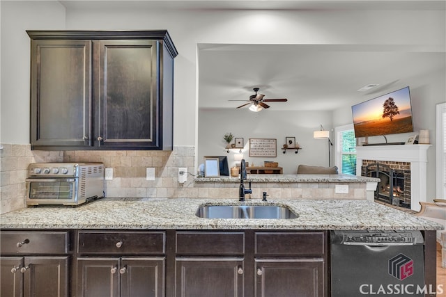 kitchen with dark brown cabinetry, dishwashing machine, a peninsula, and a sink