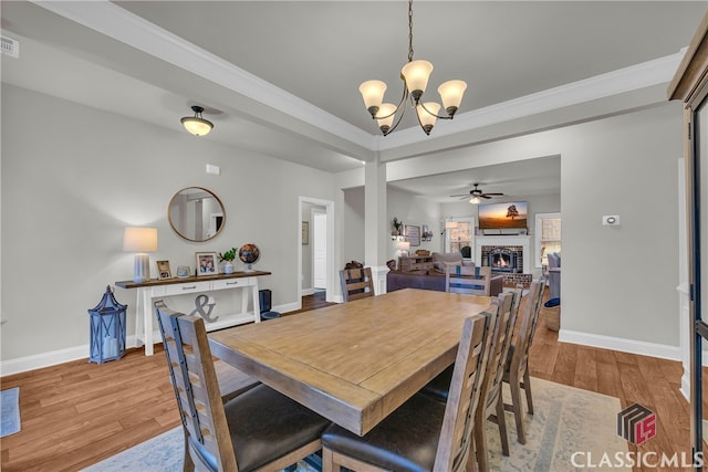 dining space featuring ornamental molding, a brick fireplace, wood finished floors, baseboards, and ceiling fan with notable chandelier