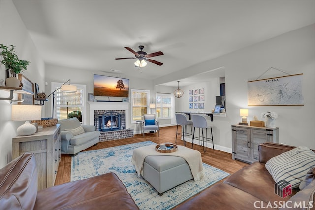 living room with ceiling fan, a fireplace, baseboards, and wood finished floors