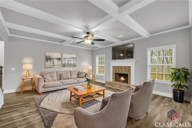 living room with beamed ceiling, plenty of natural light, light hardwood / wood-style floors, and a brick fireplace