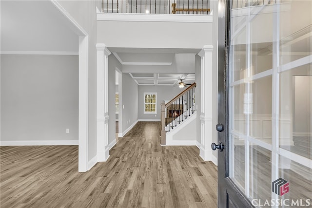 foyer entrance with decorative columns, crown molding, coffered ceiling, and light wood-type flooring