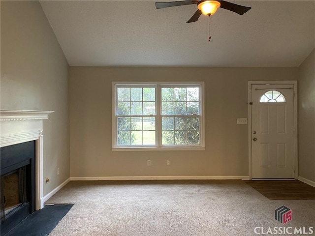 unfurnished living room with ceiling fan, dark carpet, and vaulted ceiling