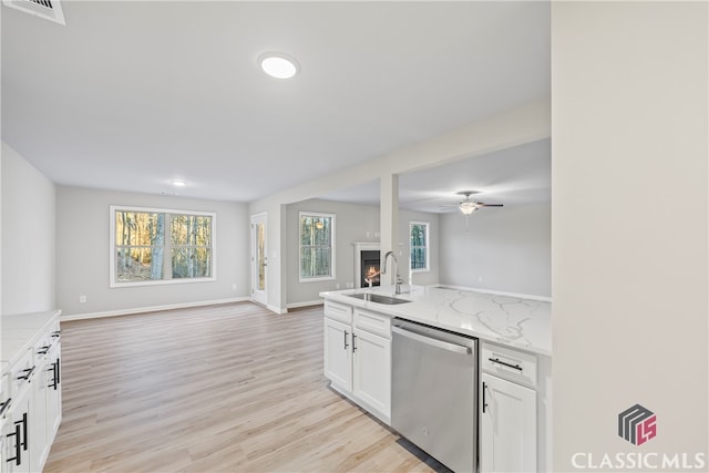 kitchen featuring light stone countertops, stainless steel dishwasher, a wealth of natural light, sink, and white cabinets