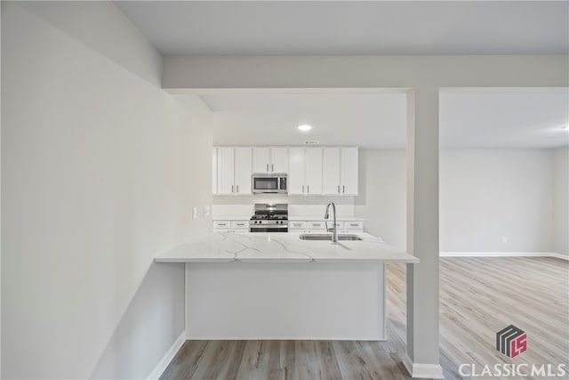 kitchen with white cabinetry, sink, kitchen peninsula, light hardwood / wood-style floors, and appliances with stainless steel finishes