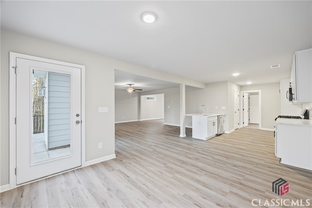 unfurnished living room featuring a wealth of natural light, ceiling fan, sink, and light wood-type flooring