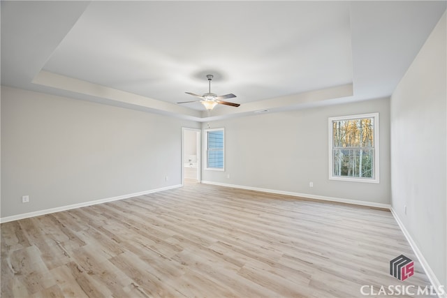 spare room with light hardwood / wood-style floors, a raised ceiling, and ceiling fan