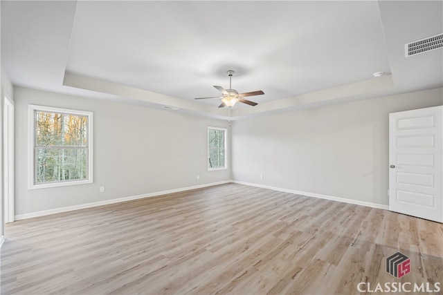 empty room featuring a raised ceiling, ceiling fan, and light hardwood / wood-style flooring