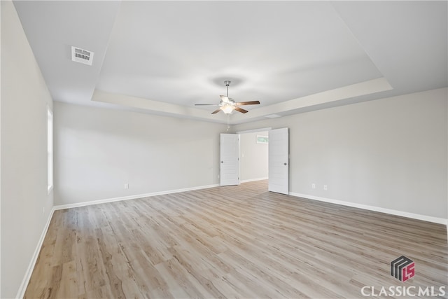 spare room with ceiling fan, a raised ceiling, and light wood-type flooring